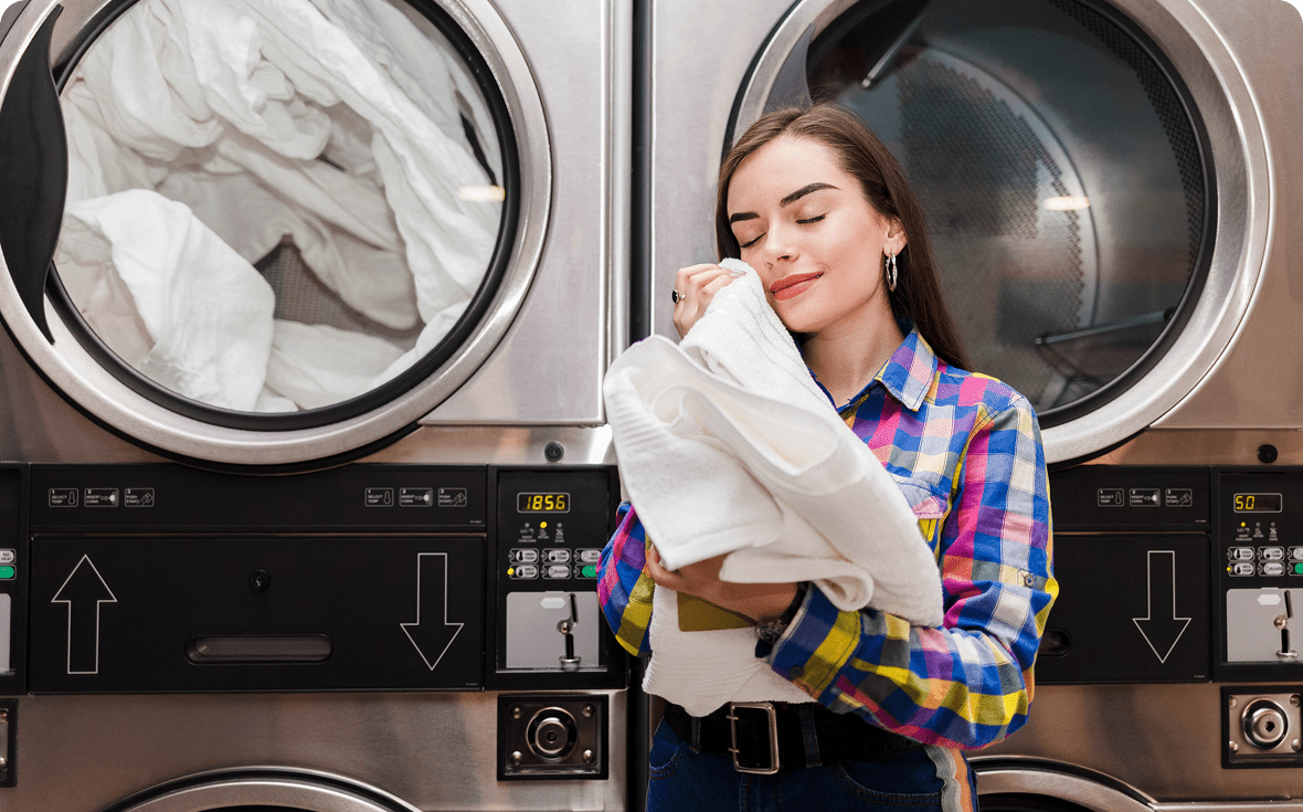 A woman happily holding fresh laundry in a laundromat.