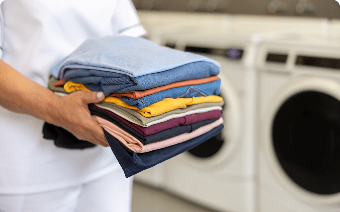 Person holding neatly folded colorful clothes in a laundry room.