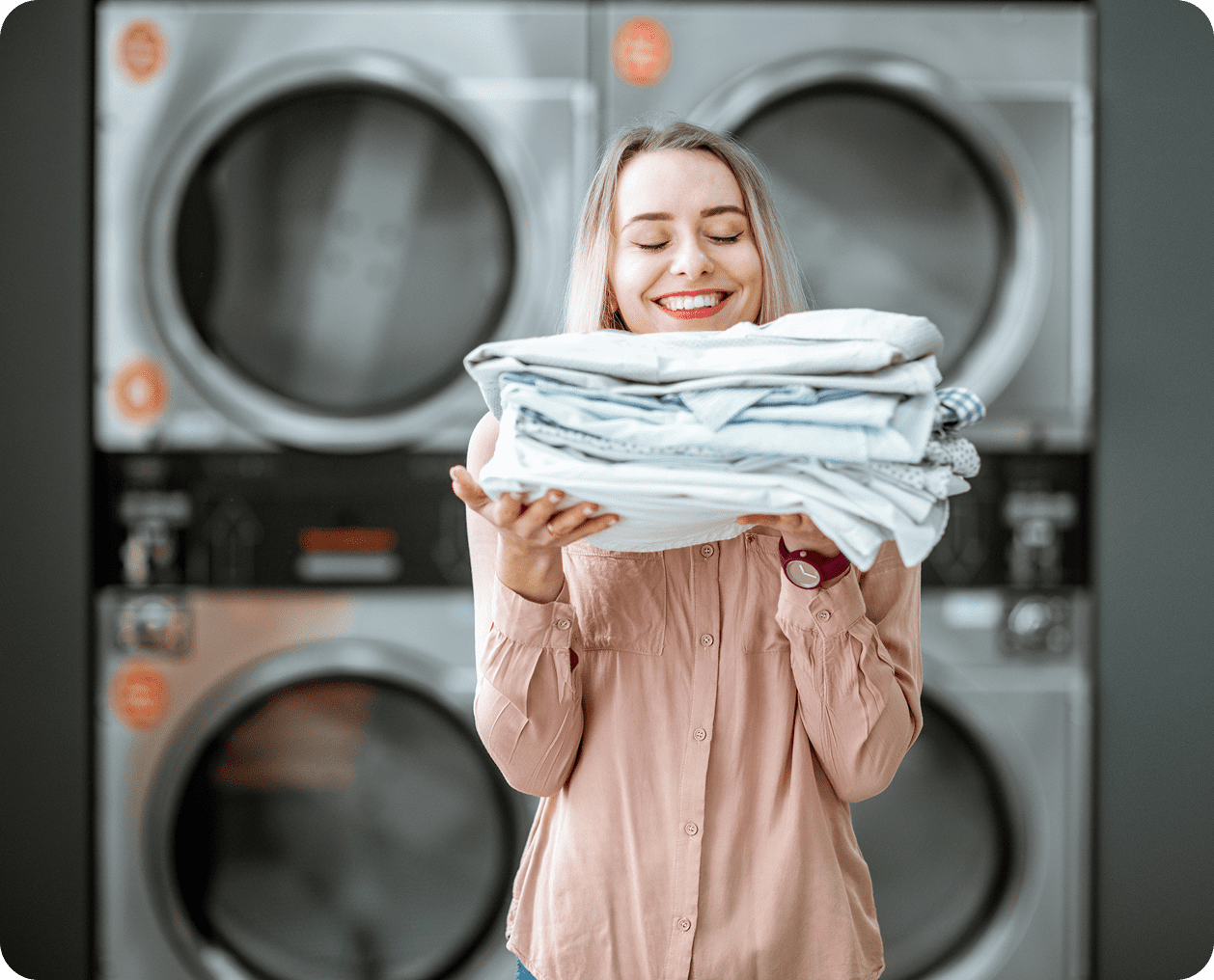 Woman happily holding a stack of clean towels in a laundromat.