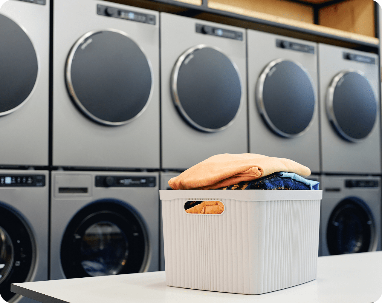Laundry basket with clothes in front of washing machines.