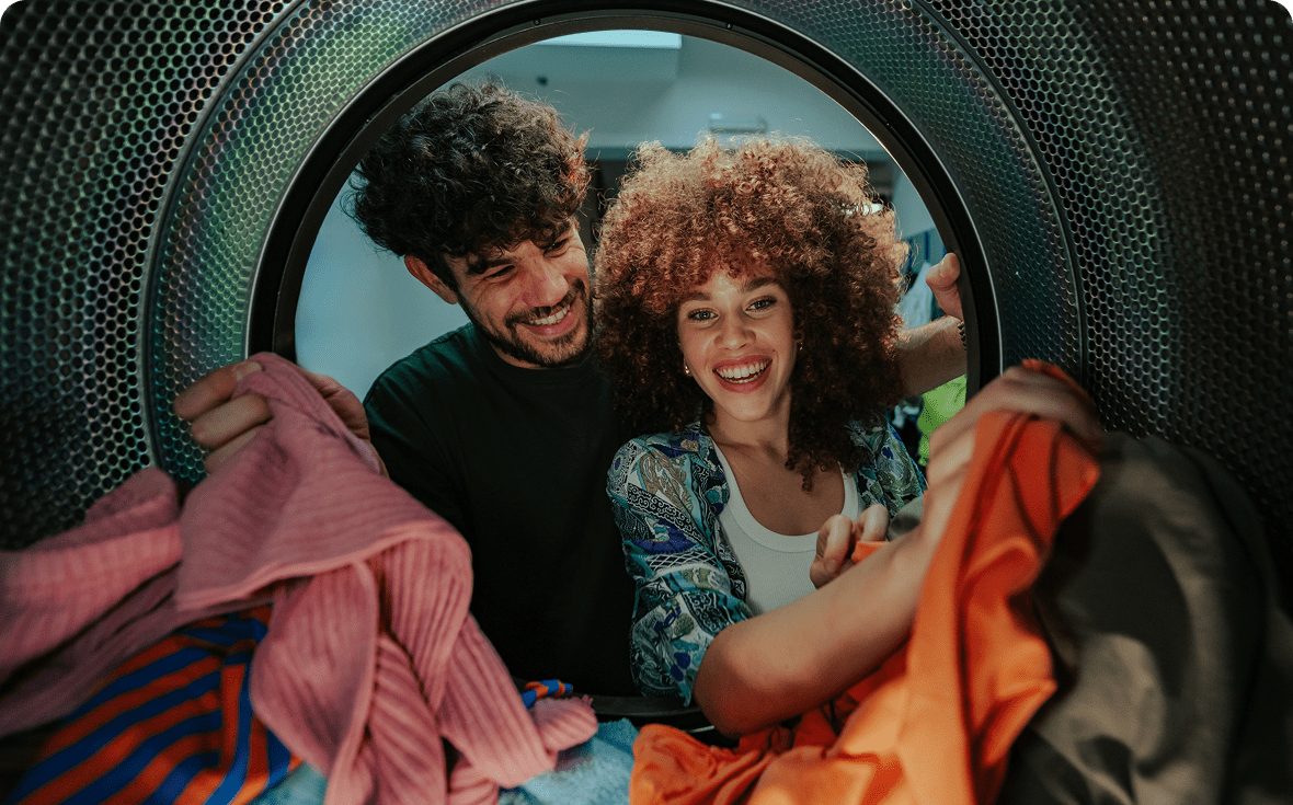 Happy couple sorting colorful laundry inside a washing machine.